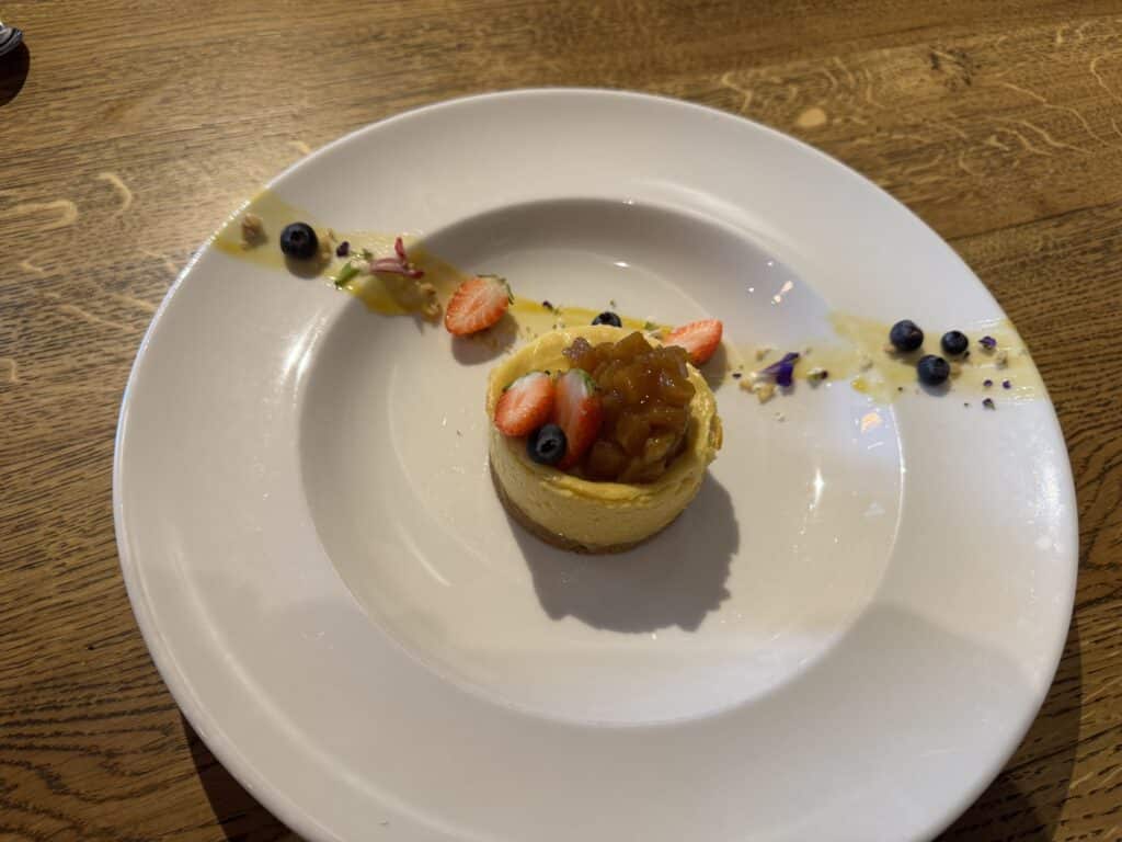 Mini cheesecake joliment dressé sur assiette blanche, garni de compote de fruits, fraises, myrtilles et sauce mangue. Sur table en bois.