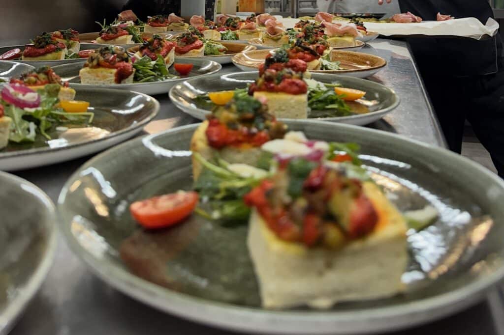 Multiples assiettes de canapés d'antipasti, probablement de la polenta ou du pain garnis de légumes grillés, prêts pour le service en cuisine professionnelle.